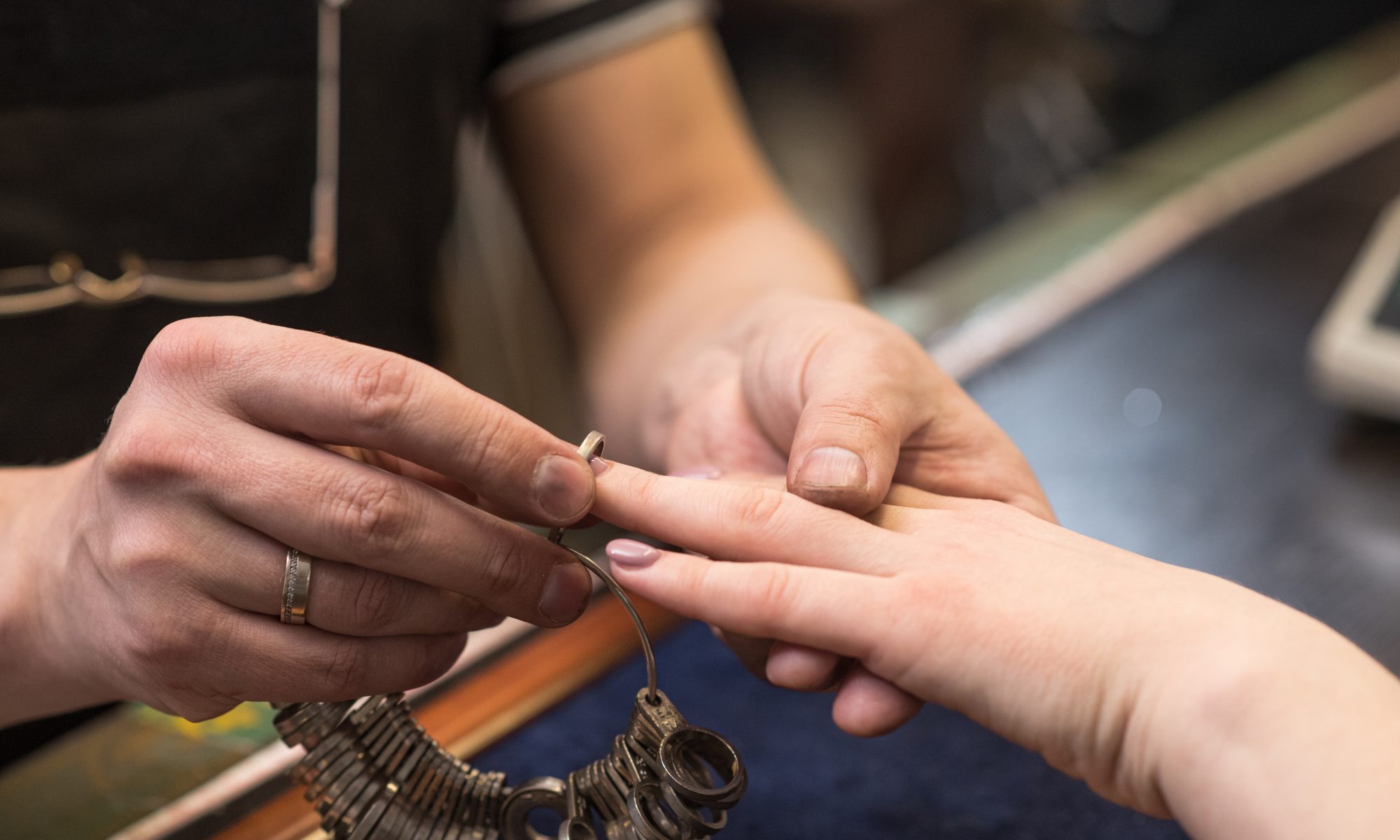 A jeweler checking the ring size of a woman, when designing Custom Engagement Ring St. John.